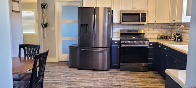 kitchen with sink, wood-type flooring, white cabinets, stainless steel appliances, and backsplash