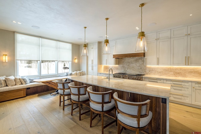 kitchen featuring an island with sink, custom range hood, sink, and decorative light fixtures