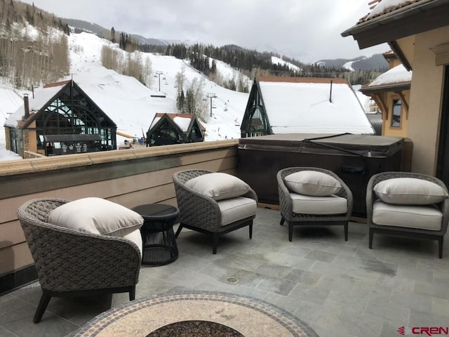 snow covered patio with a hot tub and a mountain view