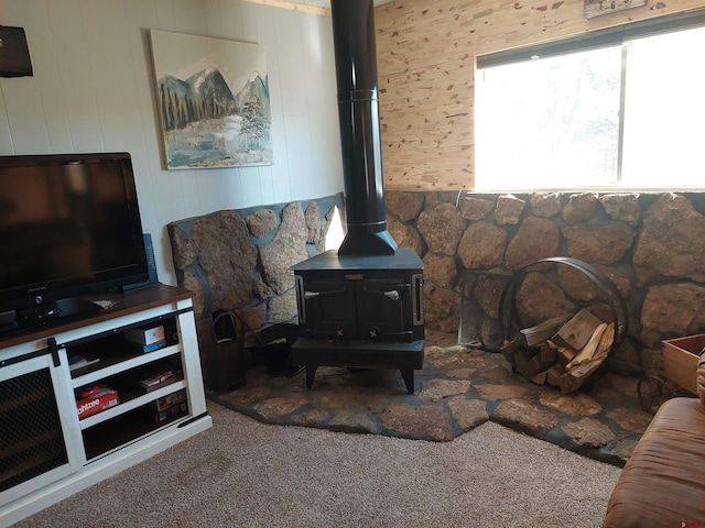 carpeted living room with wood walls and a wood stove