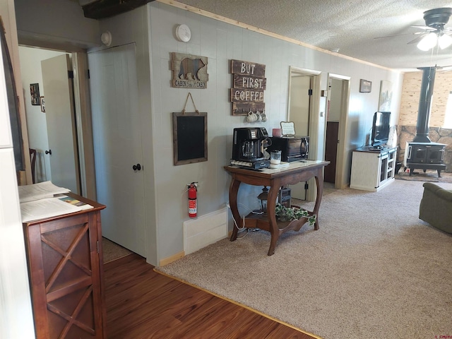 interior space with ceiling fan, carpet, a textured ceiling, and a wood stove