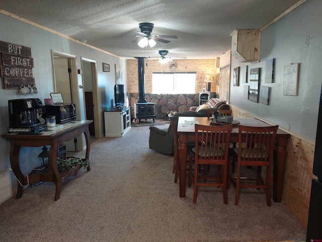 carpeted dining room featuring crown molding, wooden walls, a textured ceiling, and a wood stove