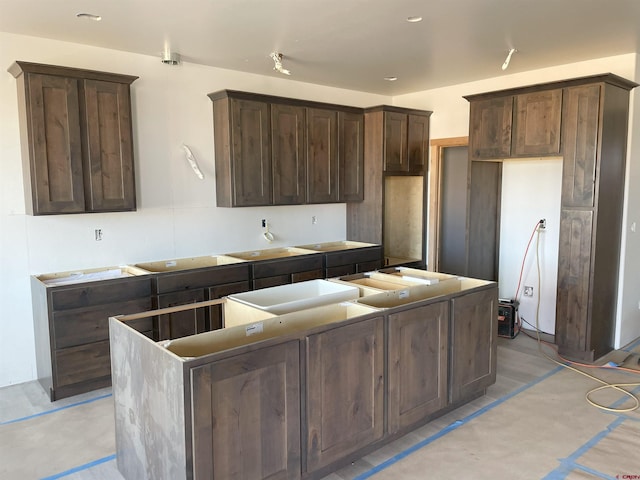 kitchen featuring dark brown cabinets, a center island, concrete flooring, and stovetop