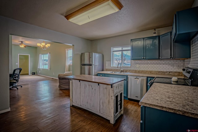 kitchen featuring blue cabinetry, wall chimney exhaust hood, sink, appliances with stainless steel finishes, and pendant lighting