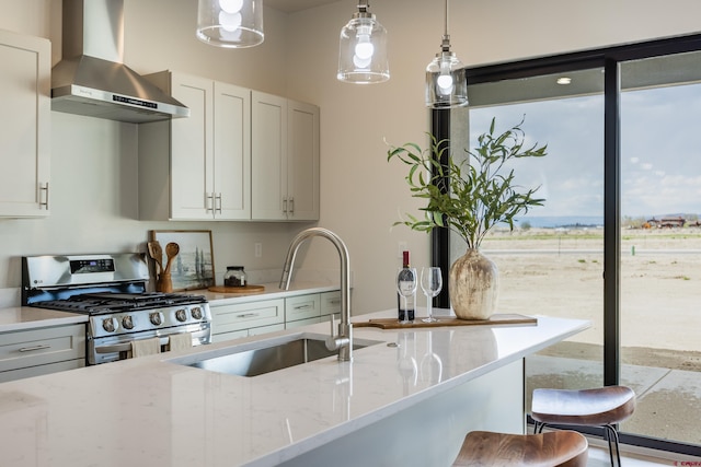 kitchen featuring stainless steel gas stove, white cabinetry, sink, light stone counters, and wall chimney range hood