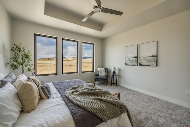 carpeted bedroom with a raised ceiling and ceiling fan