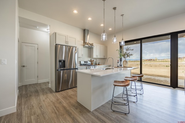 kitchen featuring sink, white cabinets, wall chimney range hood, stainless steel appliances, and a center island with sink