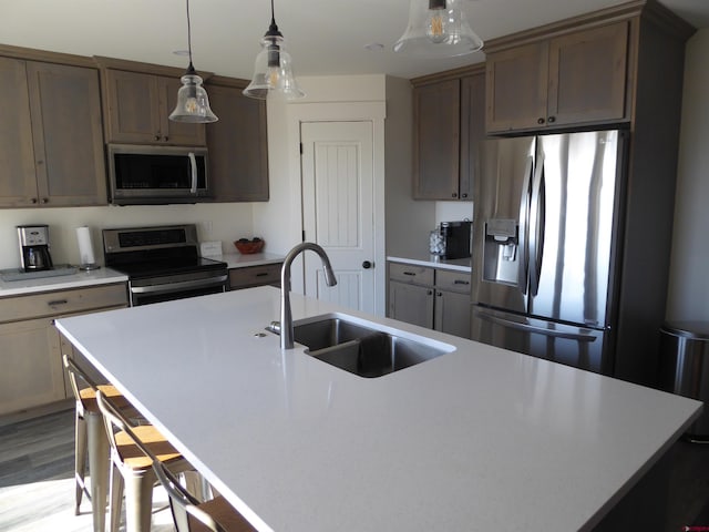 kitchen with sink, decorative light fixtures, appliances with stainless steel finishes, an island with sink, and light hardwood / wood-style floors