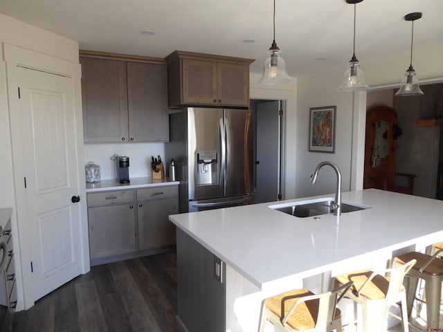 kitchen featuring stainless steel refrigerator with ice dispenser, a breakfast bar, sink, hanging light fixtures, and an island with sink