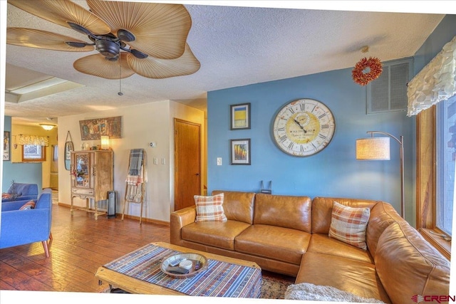 living room featuring dark wood-type flooring, ceiling fan, and a textured ceiling