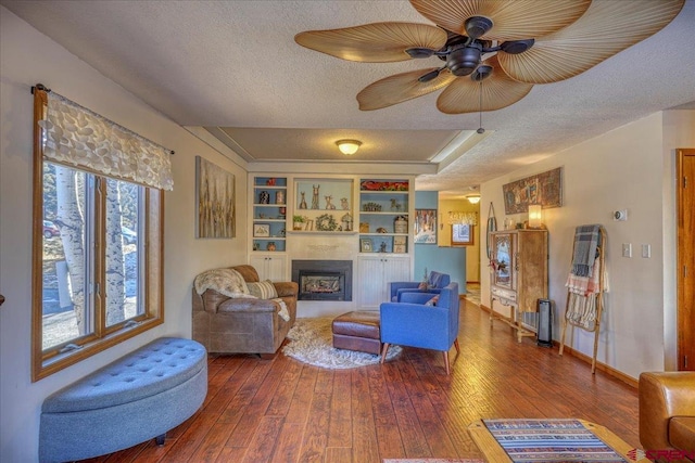 living room featuring hardwood / wood-style flooring, ceiling fan, a textured ceiling, and built in shelves