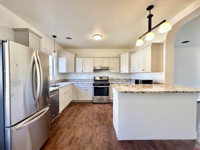 kitchen featuring stainless steel appliances, white cabinets, light stone counters, and decorative light fixtures