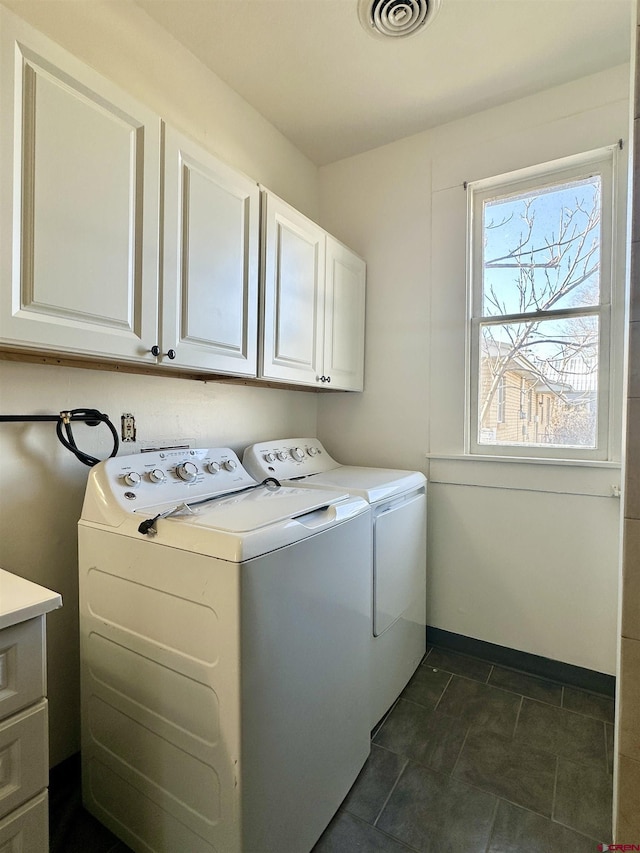 clothes washing area with cabinets, dark tile patterned floors, and washer and clothes dryer