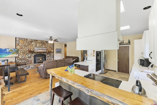 dining space featuring a stone fireplace, sink, ceiling fan, and light hardwood / wood-style floors