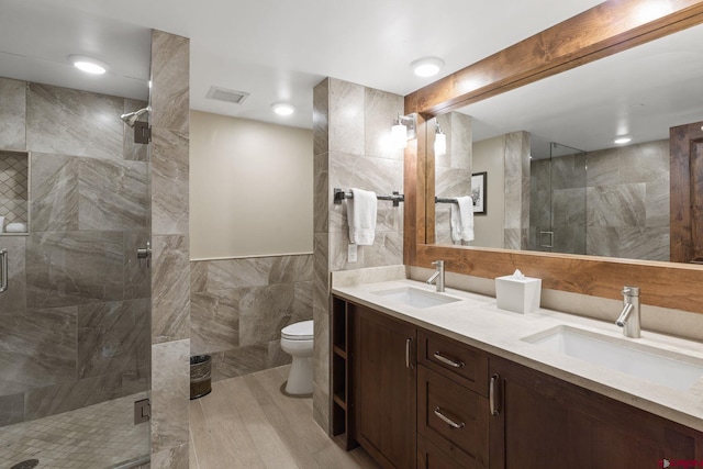 bathroom with tile walls, vanity, toilet, and an enclosed shower