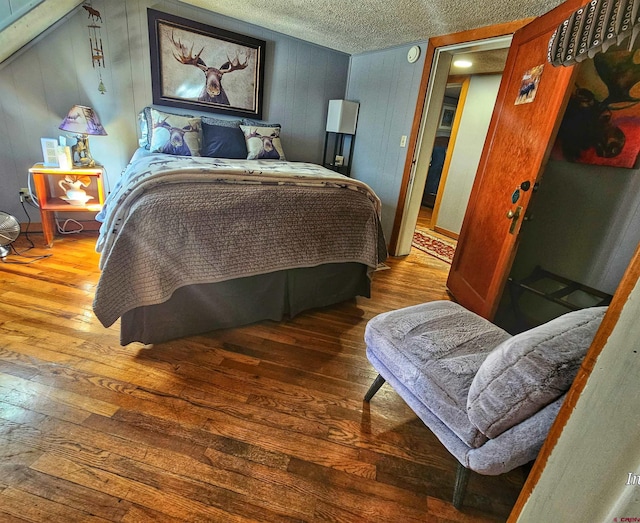 bedroom featuring wood-type flooring, wooden walls, and a textured ceiling