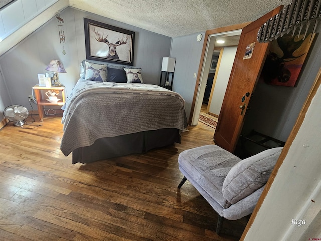 bedroom with wood-type flooring, vaulted ceiling, and a textured ceiling