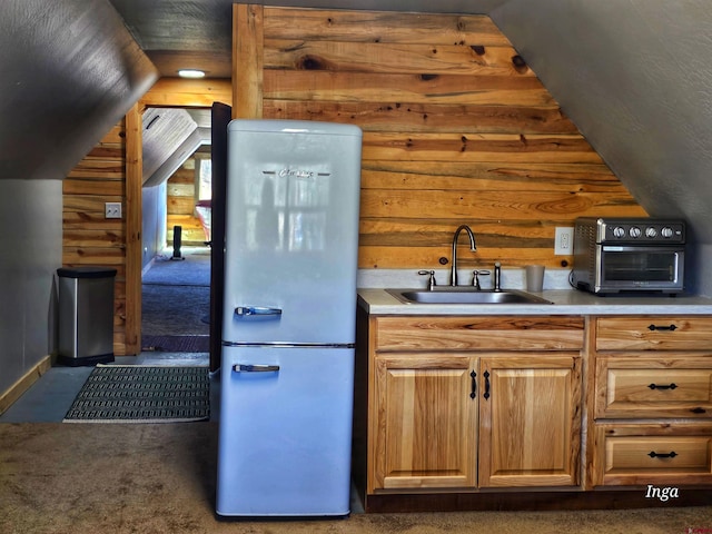 kitchen with lofted ceiling, sink, dark colored carpet, wood walls, and fridge