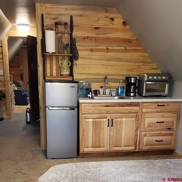 kitchen featuring light brown cabinetry, sink, wood walls, vaulted ceiling, and stainless steel fridge