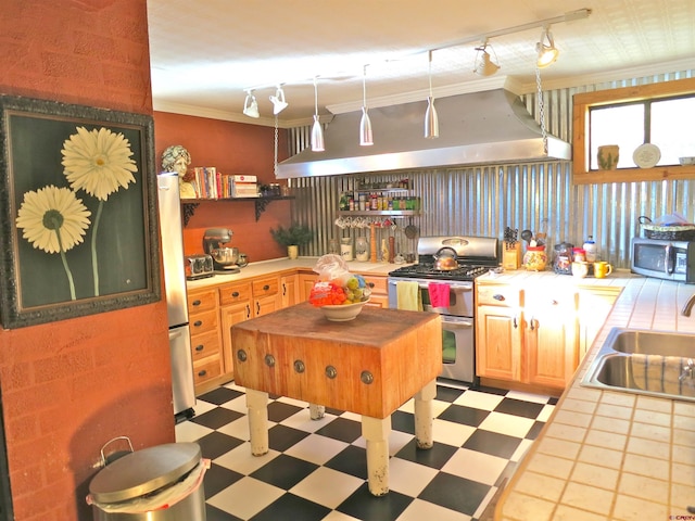 kitchen with wall chimney exhaust hood, sink, crown molding, tile countertops, and stainless steel appliances