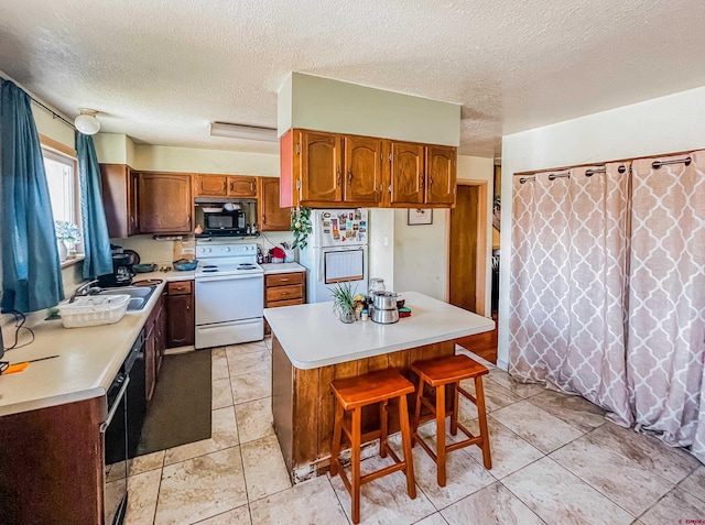 kitchen with sink, white appliances, a breakfast bar, a textured ceiling, and a kitchen island