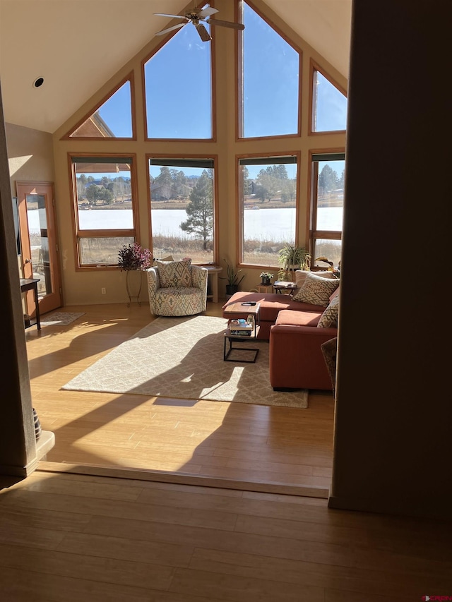 living room featuring ceiling fan, a water view, high vaulted ceiling, and light hardwood / wood-style floors