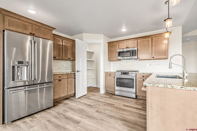 kitchen with appliances with stainless steel finishes, decorative light fixtures, sink, light stone countertops, and light wood-type flooring