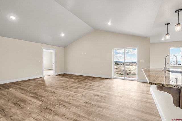 unfurnished living room featuring lofted ceiling, sink, and light hardwood / wood-style floors