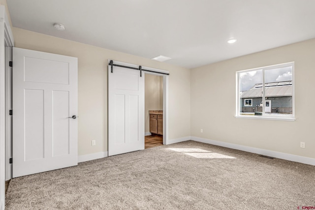 unfurnished bedroom with ensuite bath, a barn door, and carpet