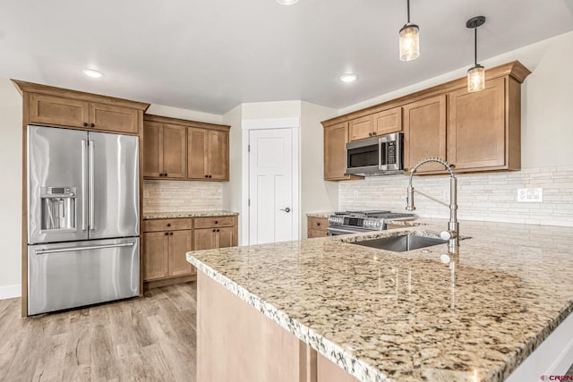 kitchen featuring sink, premium appliances, hanging light fixtures, light stone counters, and light wood-type flooring