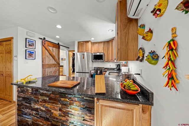 kitchen with sink, light wood-type flooring, dark stone countertops, stainless steel appliances, and a barn door