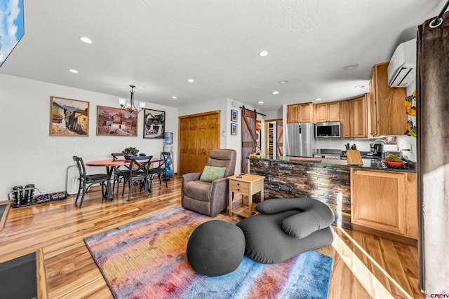 living room with sink, an inviting chandelier, light hardwood / wood-style floors, a barn door, and an AC wall unit