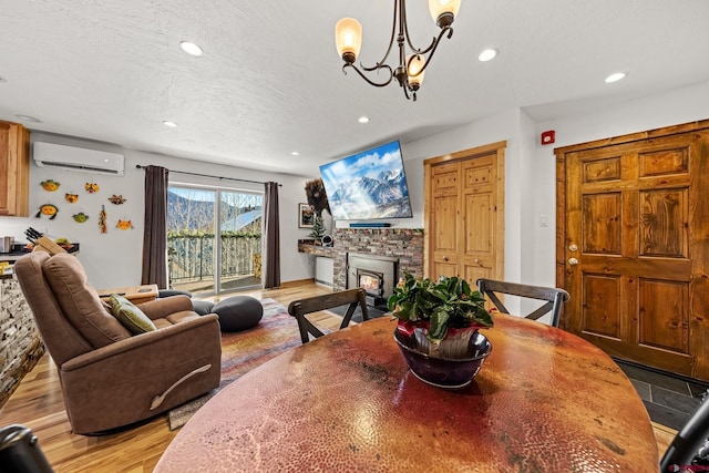 dining room featuring an AC wall unit, a fireplace, hardwood / wood-style flooring, a notable chandelier, and a textured ceiling