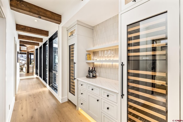 interior space with wine cooler, light hardwood / wood-style flooring, white cabinets, beamed ceiling, and backsplash