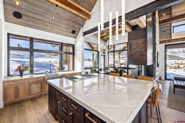 kitchen with stainless steel gas cooktop, sink, hanging light fixtures, a kitchen island, and light stone countertops