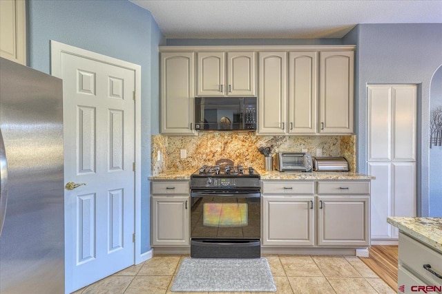 kitchen featuring tasteful backsplash, light stone countertops, light tile patterned floors, and black appliances