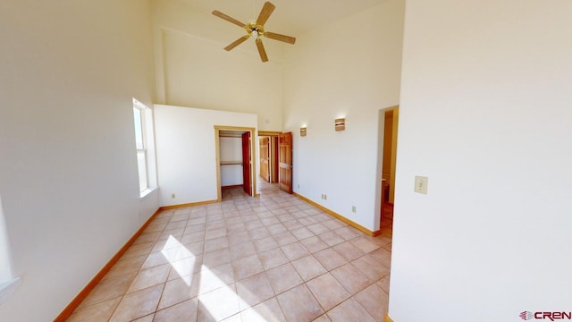 tiled empty room with ceiling fan and a high ceiling