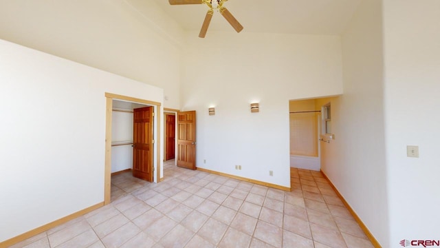 unfurnished bedroom featuring ceiling fan, a towering ceiling, a spacious closet, and light tile patterned floors