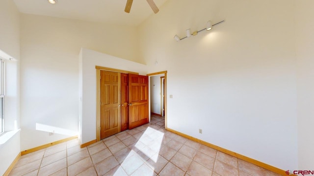 tiled spare room with ceiling fan and a towering ceiling