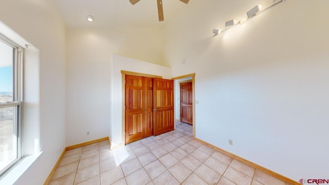 tiled empty room featuring ceiling fan and a towering ceiling