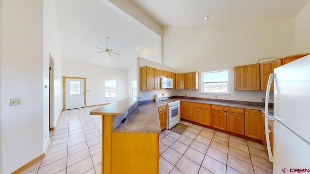 kitchen with light tile patterned flooring, ceiling fan, kitchen peninsula, white appliances, and beam ceiling