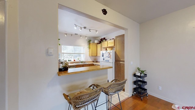 kitchen with a kitchen bar, sink, kitchen peninsula, white fridge, and hardwood / wood-style flooring