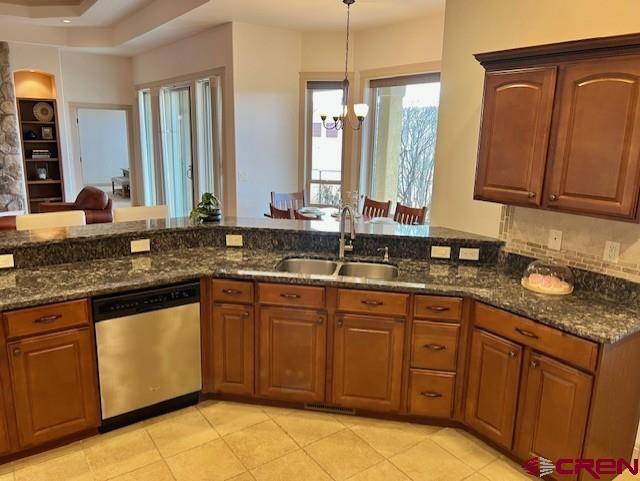 kitchen with pendant lighting, stainless steel dishwasher, sink, and dark stone countertops