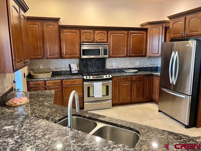 kitchen featuring stainless steel appliances, sink, dark stone countertops, and decorative backsplash