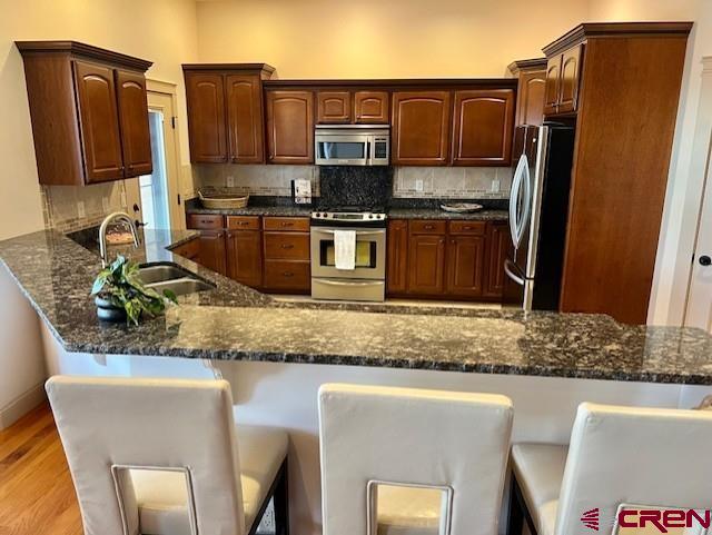 kitchen with sink, light hardwood / wood-style flooring, appliances with stainless steel finishes, dark stone countertops, and decorative backsplash