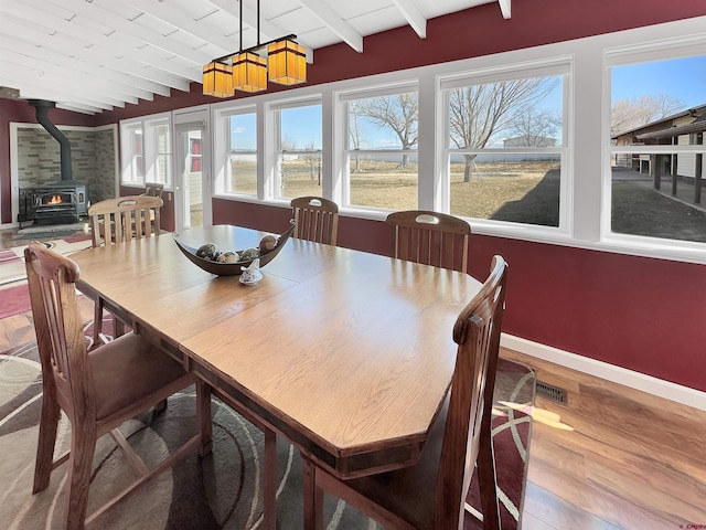 dining space with vaulted ceiling with beams, wood ceiling, wood-type flooring, and a wood stove