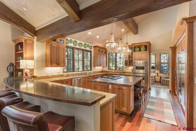 kitchen with a kitchen island, appliances with stainless steel finishes, pendant lighting, wood-type flooring, and a kitchen breakfast bar