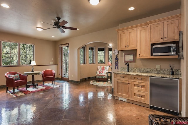 kitchen with fridge, ceiling fan, light stone counters, and light brown cabinets