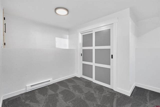 unfurnished room featuring baseboard heating, baseboards, and dark carpet