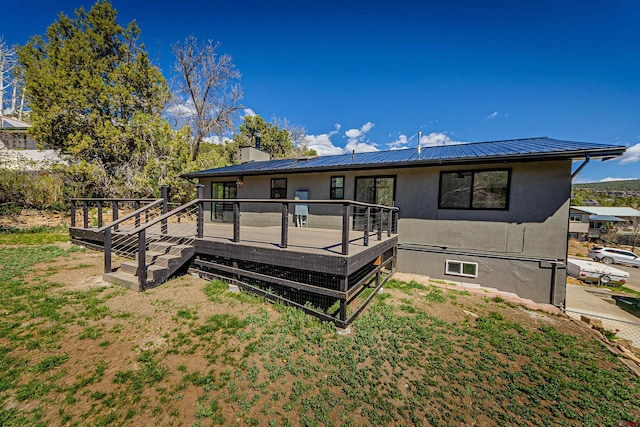 rear view of property featuring a wooden deck, stucco siding, a chimney, and metal roof
